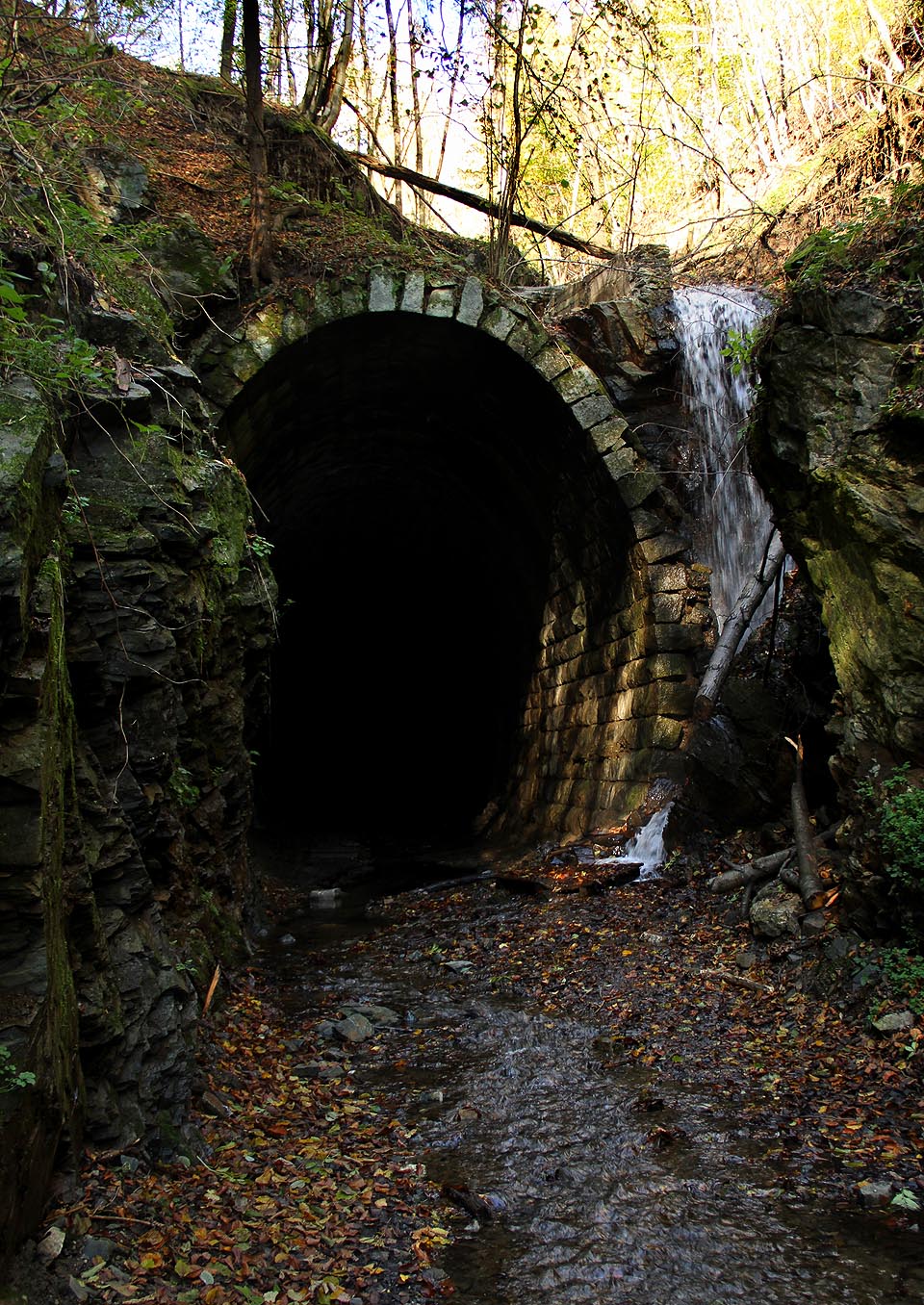 Mníšanský potok spadá přímo po kamenné klenbě tunelu, který naplňuje jemnou vodní tříští.