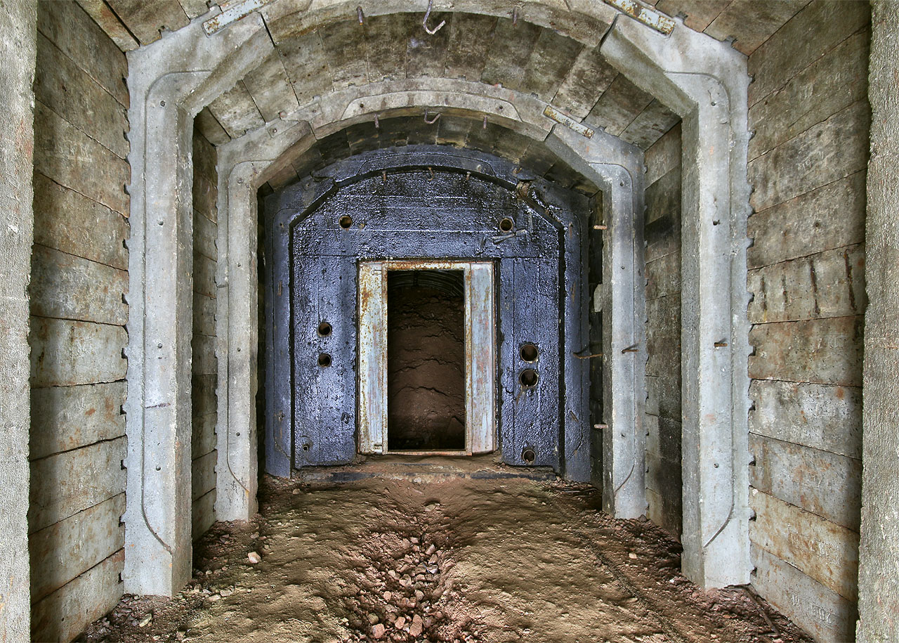 Protilehlá chodba nabízí pohled na betonovou stěnu načerněnou dehtem, za kterou se zřejmě kdysi skrýval nebo aspoň skrývat měl, nouzový východ - tedy šachta vedoucí vzhůru k povrchu.