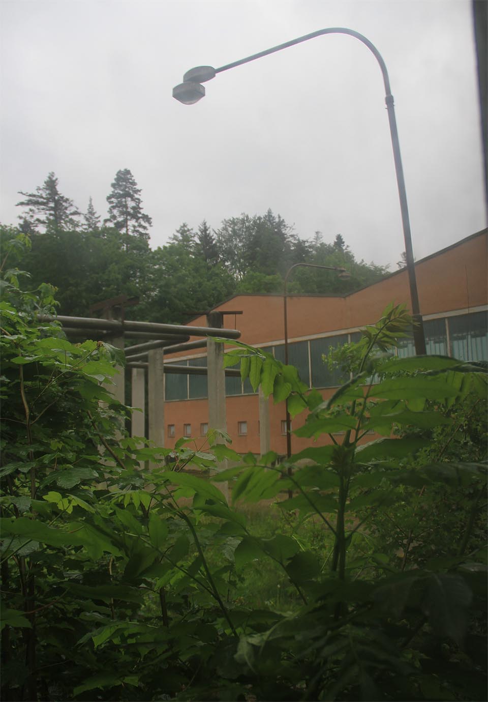 Poslední rozloučení: pohled do deštivého dne na osamělé haly přes zaprášené sklo.