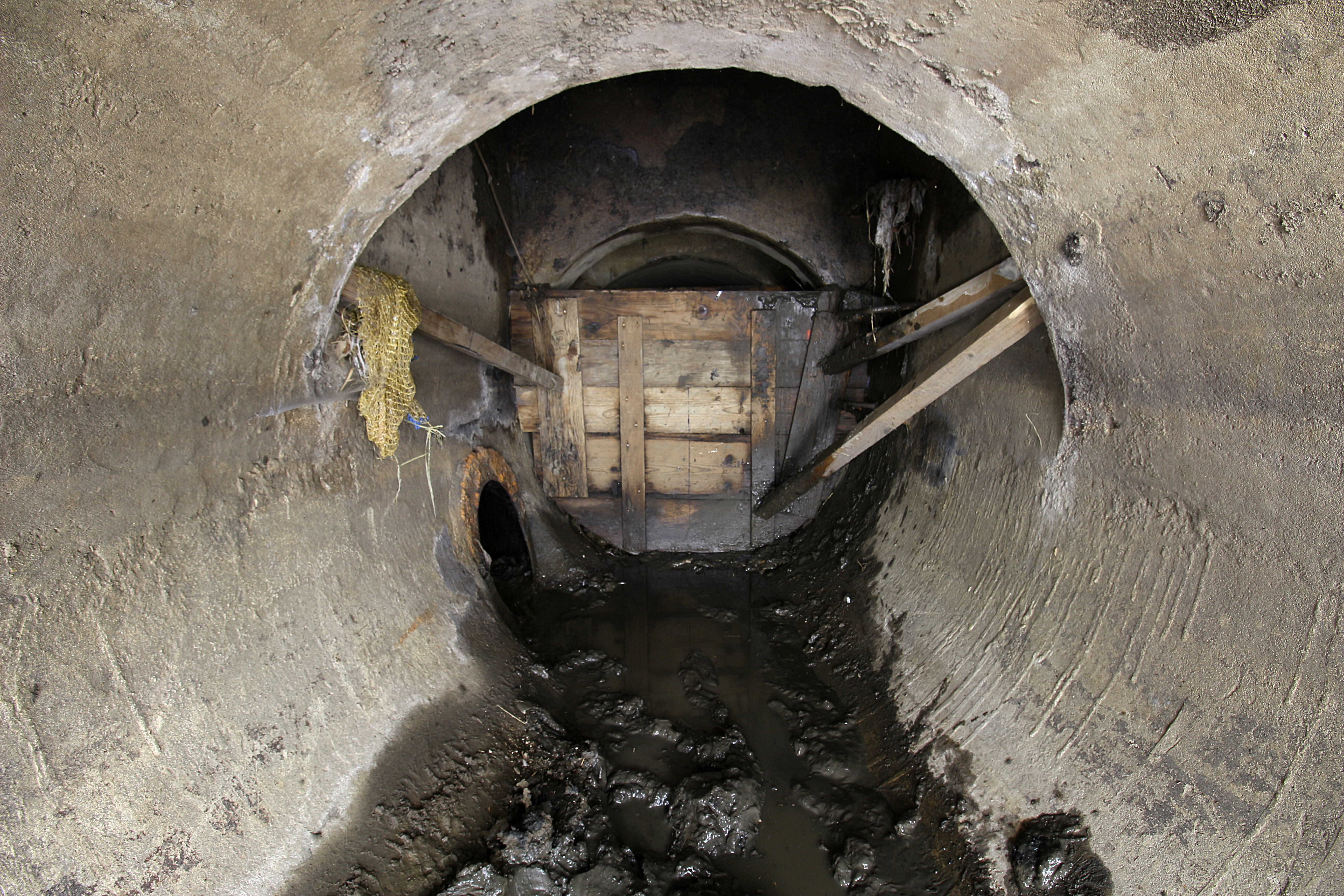 Tak vypadá závěrečná pasáž pod svitavským nábřežím. Rourou vlevo odtéká voda pod jez, dřevěná bariéra a pytle s pískem za ní oddělují stoku od hladiny řeky nad jezem. Jde nejspíš o pozůstatek po povodni ze září 2024, který dosud nebyl odstraněn a díky tomu se ve <a href="/Tema/Tunely Svitavské strouhy pod Zábrdovickou ulicí">štole</a> drží poměrně dost smrdutého bahna.