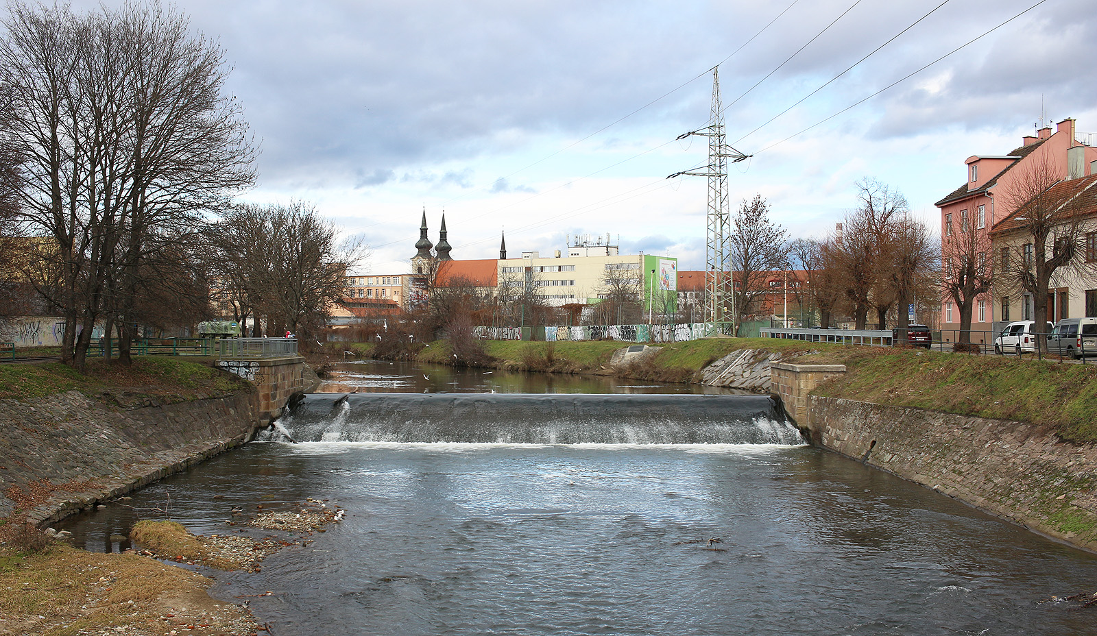Udělejme tečku za textem o Svitavské strouze při pohledu na jez za Tkalcovskou ulicí. Ačkoliv se dnes díváme zpříma na Svitavu, řeka tudy historicky nikdy neprotékala. Namísto toho proudily její vody téměř kolmo k dnešnému toku: na fotce zprava zpod mříže u úpaté stožáru vysokého napětí (ústí Svitavské strouhy) doleva pod stavidlo za zeleným zábradlím (<a href="/Tema/Svitavský náhon">Svitavský náhon</a>).