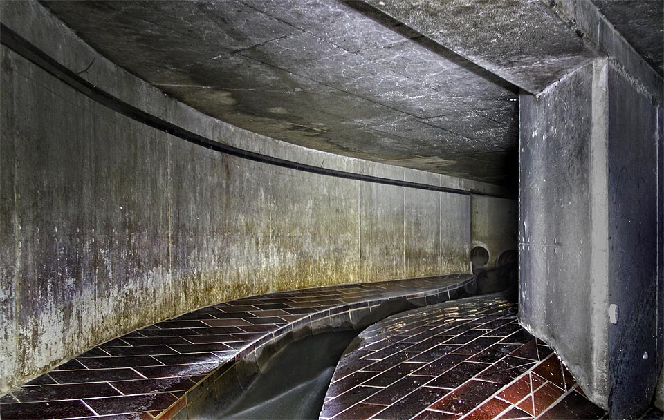 Vykachlíkovanou chodbou se voda řítí vysokou rychlostí masivní kynetou ve dně. Ke svému zklamání zjišťujeme, že přitéká <a href="/Tema/Tunely Svitavského náhonu za Špitálkou">dvojicí trub</a> tak úzkých, že se do nich nevejdeme.