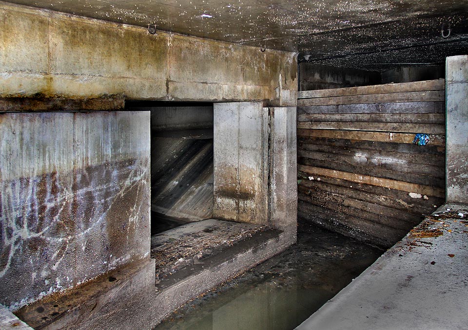 Dřevěné pažení, za kterým se valí v ostrém úhlu zatáčející a do hloubky padající splaškové vody přivaděče CB ústícího do kmenové stoky C.