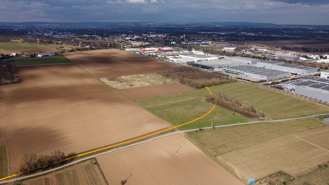 Detailní pohled na oblouk blíže Evropské ulice v Modřicích. Ani zde nezbylo po drážce takřka nic, těleso je rozorané a na místě lze nalézt jen nevýraznou terénní vlnu v travnaté ploše vpravo od středu snímku.