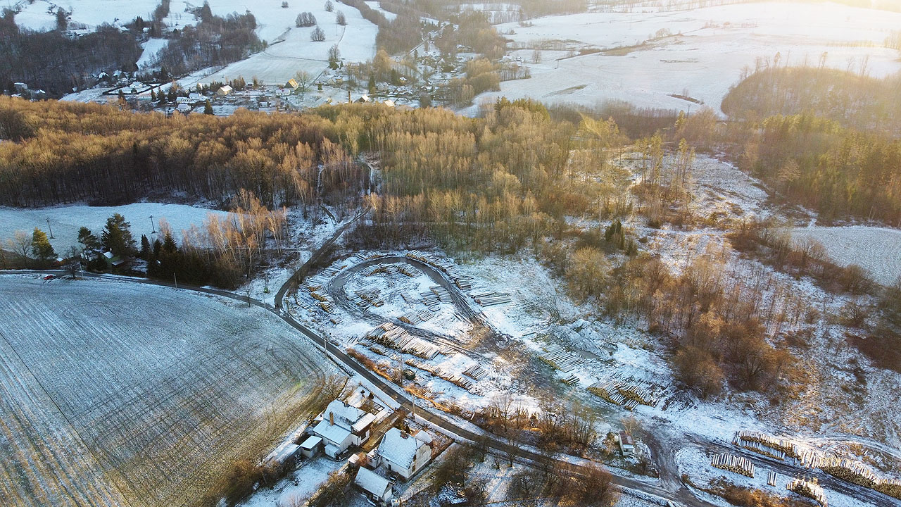 Letecký pohled na překladiště dřeva nad papírnou (ze které vykukuje komín dole v údolí). Přesto, že se již půl století v továrně papír ani celulóza nevyrábí, překladiště slouží lesníkům ke skladování dřeva dodnes.