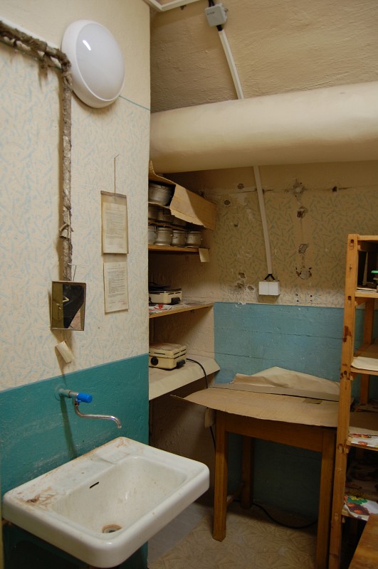 Skromná kuchyňka či přípravna jídel. Na policích leží vyrovnané ešusy, na stěně jsou zásuvky pro dva elektrické vařiče (narozdíl od plynových totiž nespotřebovávají vzduch). Elektroinstalace byla rekonstruována zhruba v roce 2001, kryt je stále udržován v provozním stavu.