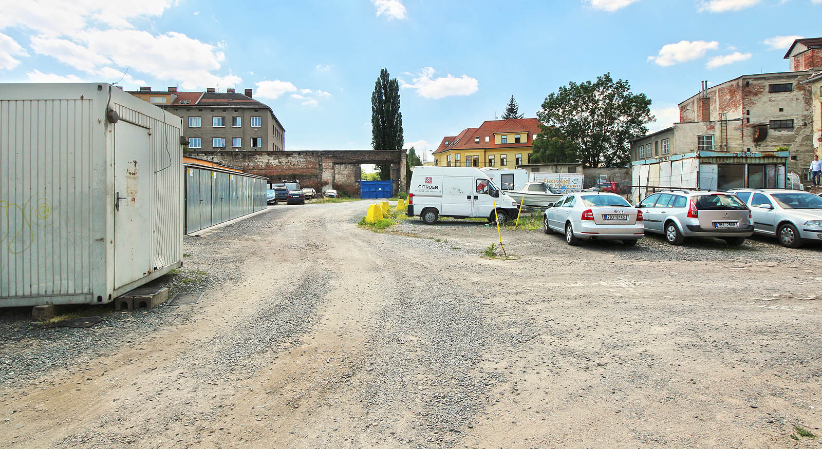 Tak vypadá skladový areál zevnitř. Vlečka do něj vcházela branou v pozadí a vedla z našeho pohledu vpravo rovnoběžně s uježděnou cestou, místem, kde stojí auta.