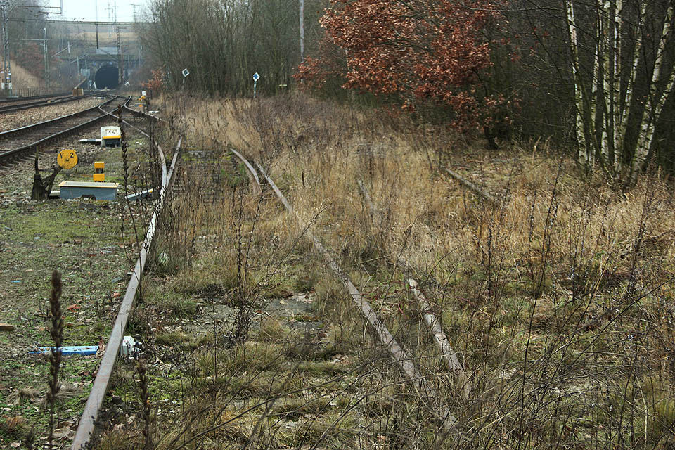 Od výhybky č. V1 pozorujeme vlevo výhybku č. V2 a ještě dále vlevo výhybku č. V3. Dvě modrá návěstidla „posun zakázán“ patří dvěma kolejím vlečky.
