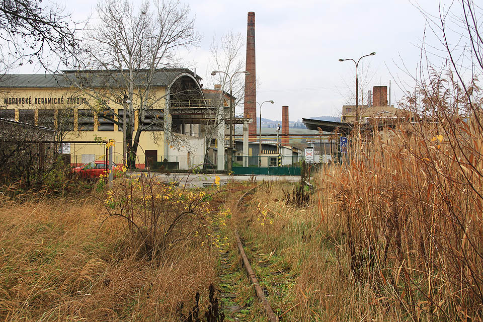 Zarostlá kolej vlečky do bývalých Moravských keramických závodů před přejezdem se silnicí č. 374 v Rájci-Jestřebí.