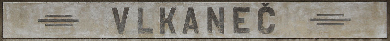 Historická cedule s názvem železniční stanice vytlačeným do cementové omítky na původní výpravní budově.