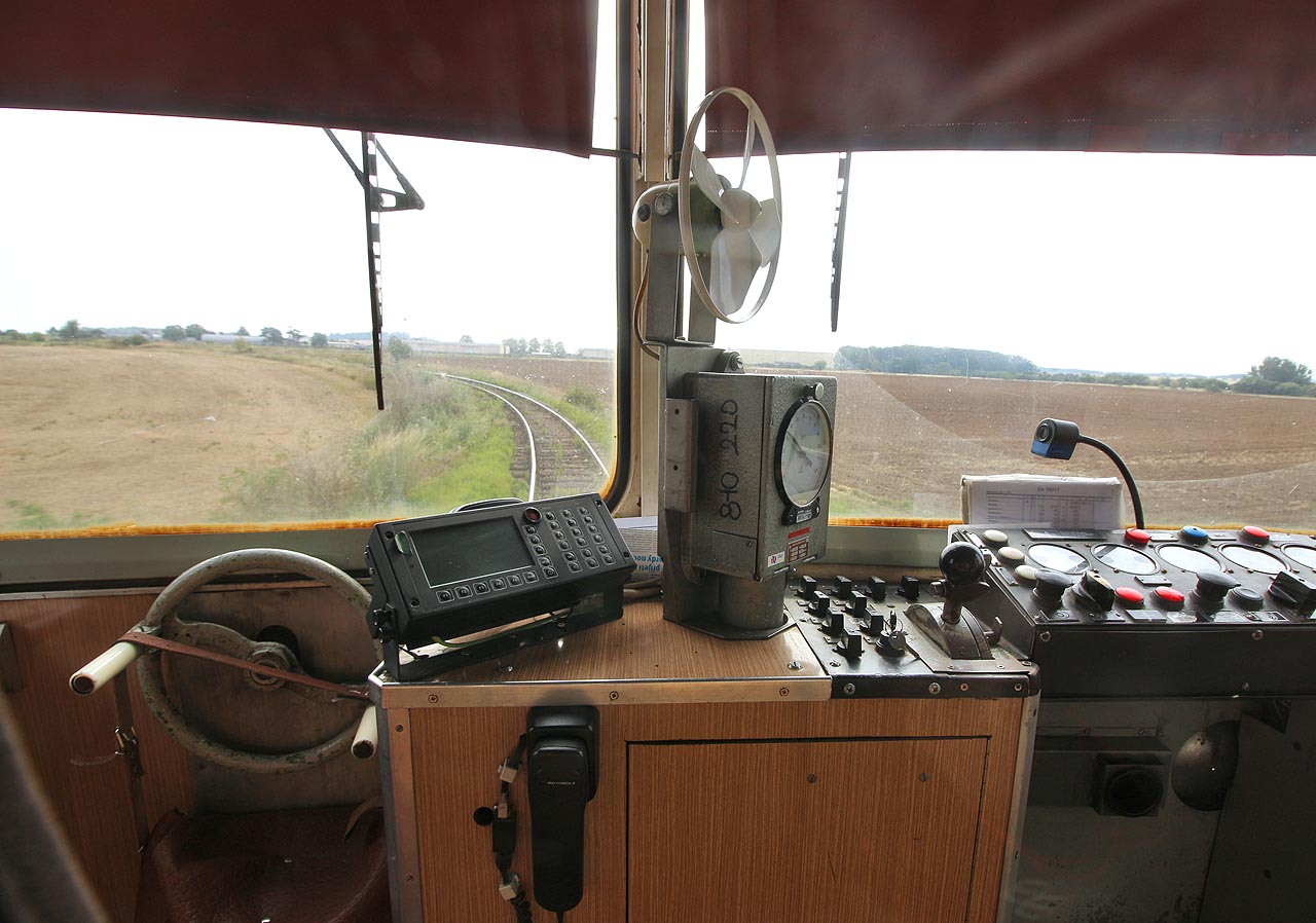 Pohled na bezútěšně plochou krajinu Polabí, jaký se nakskýtal strojvedoucím motorového vozu 810 216-2 přijíždějícího od <a href="/tema/Kouřim (žst)">Kouřimi</a> do <a href="/Tema/Bečváry (žst)">Bečvár</a> na trati Pečky–Kouřim v červenci roku 2018. Dráha tehdy ještě nesla označení číslem 013. Na obzoru je vidět skladiště Správy státních hmotných rezerv Boletex Bošice.